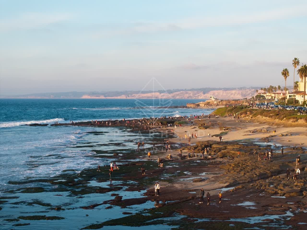 Elevated view of the beach, the surf and palm trees at La Jolla Cove, with people walking.