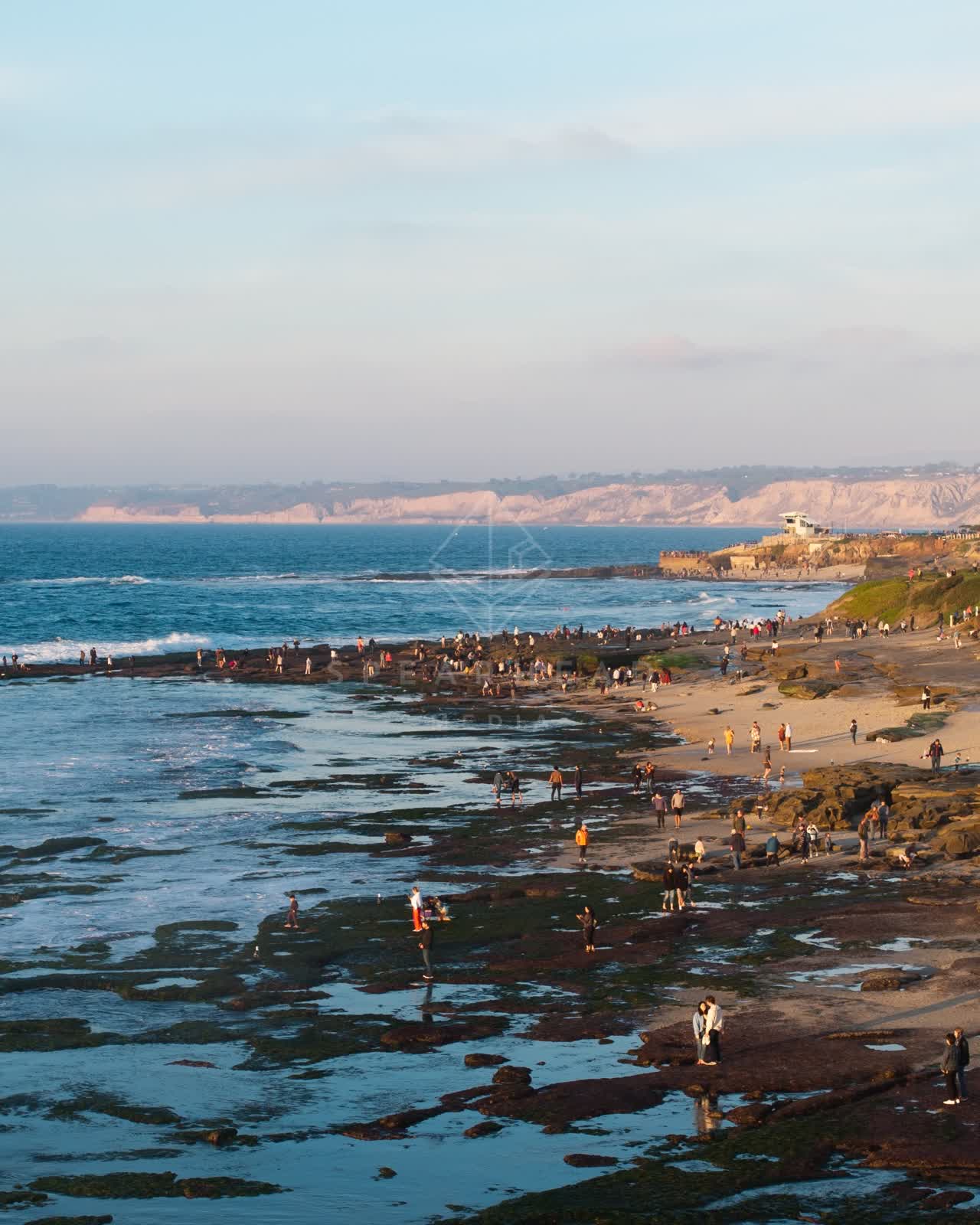 Low aerial view of the beach, the surf and the ocean at La Jolla Cove, with people walking.