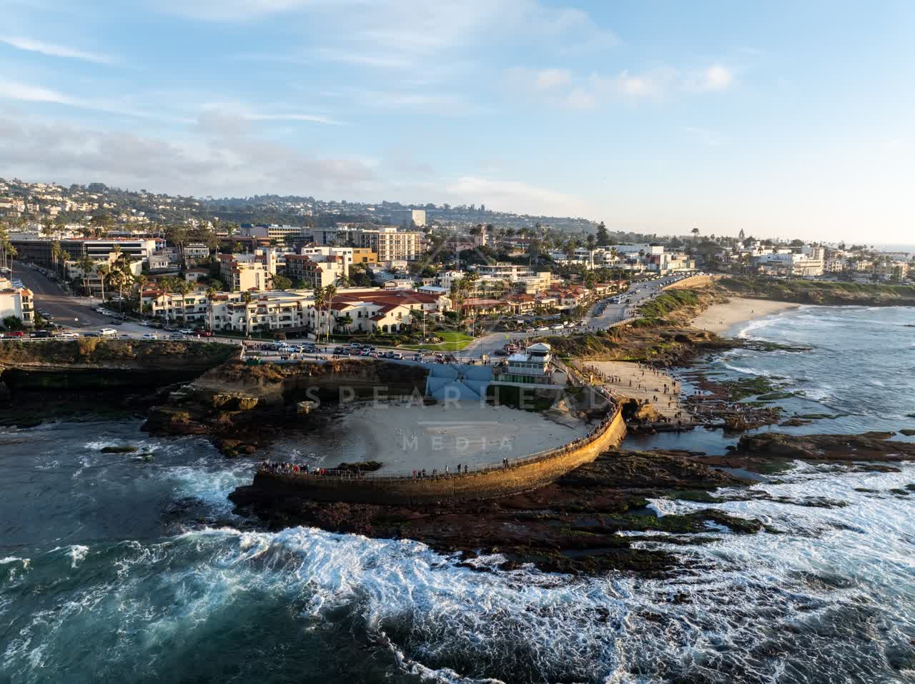 Aerial view of the cliffs, the surf and palm trees at La Jolla Cove, with people walking.