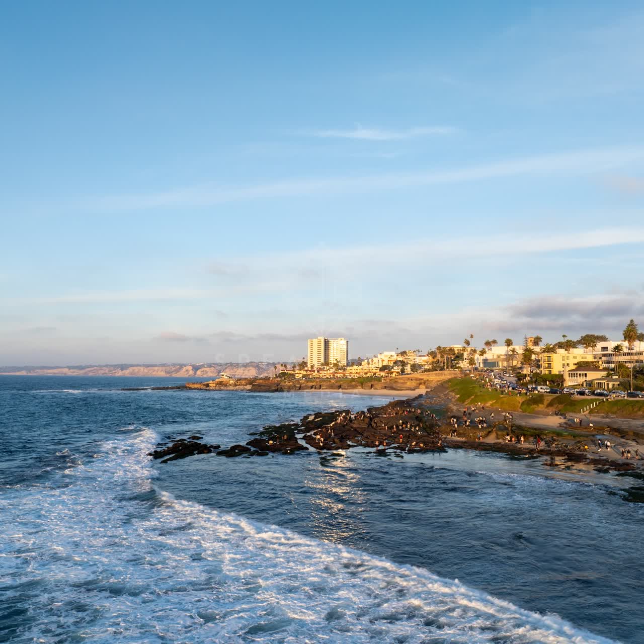 Aerial view of the cliffs, the surf and the ocean at La Jolla Cove, with a crowd gathered.