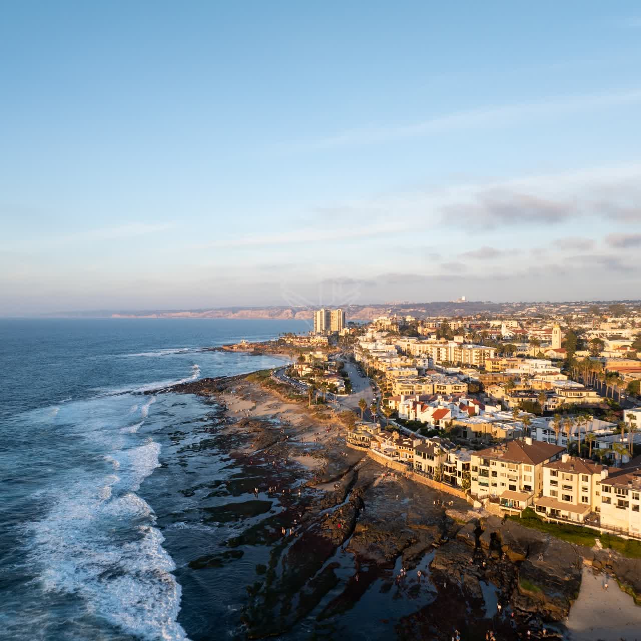 Aerial view of the cliffs, the surf and the ocean at La Jolla Cove, with people walking.