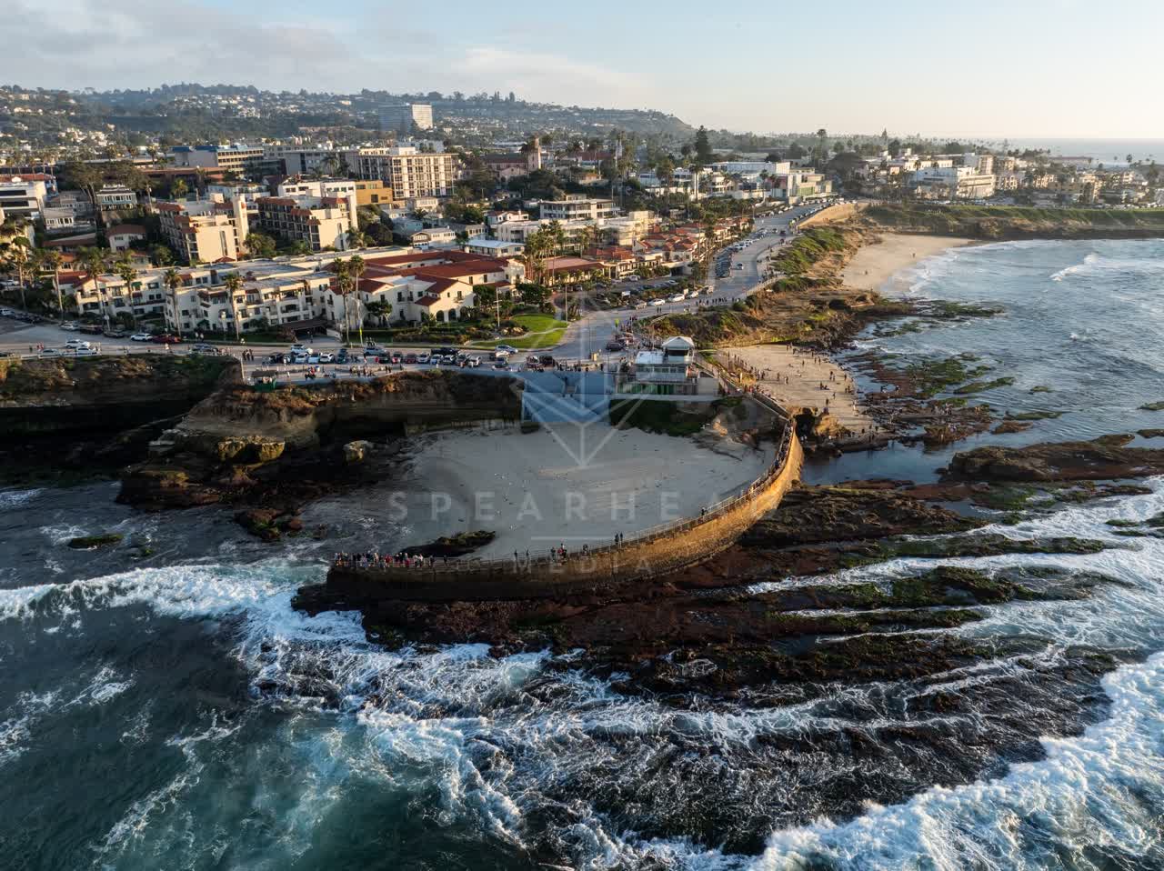 Aerial view of the cliffs, the surf and boats at La Jolla Cove, with people walking.