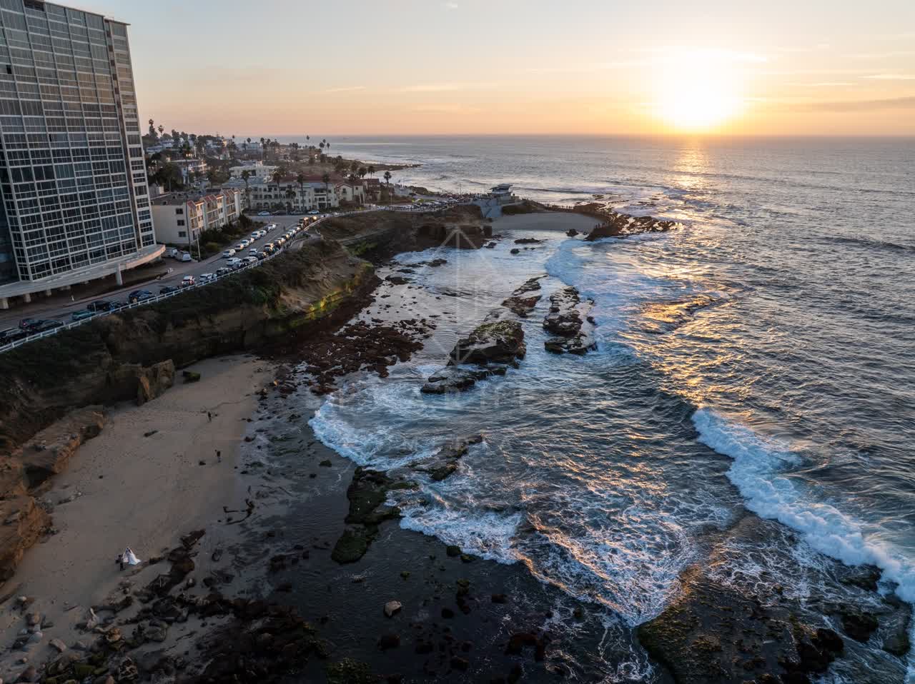 Aerial view of the cliffs, the surf and the ocean at La Jolla Cove, with people walking.
