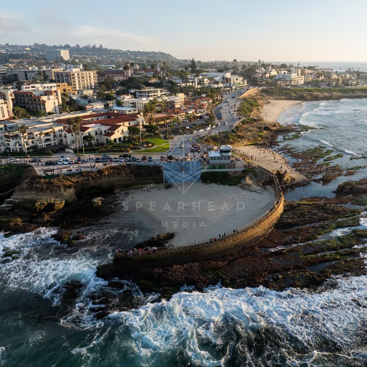 Aerial view of the cliffs, the surf and palm trees at La Jolla Cove, with people walking.