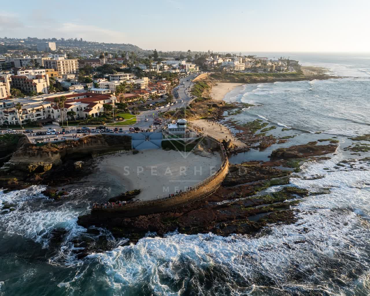 Aerial view of the cliffs, the surf and palm trees at La Jolla Cove, with people walking.