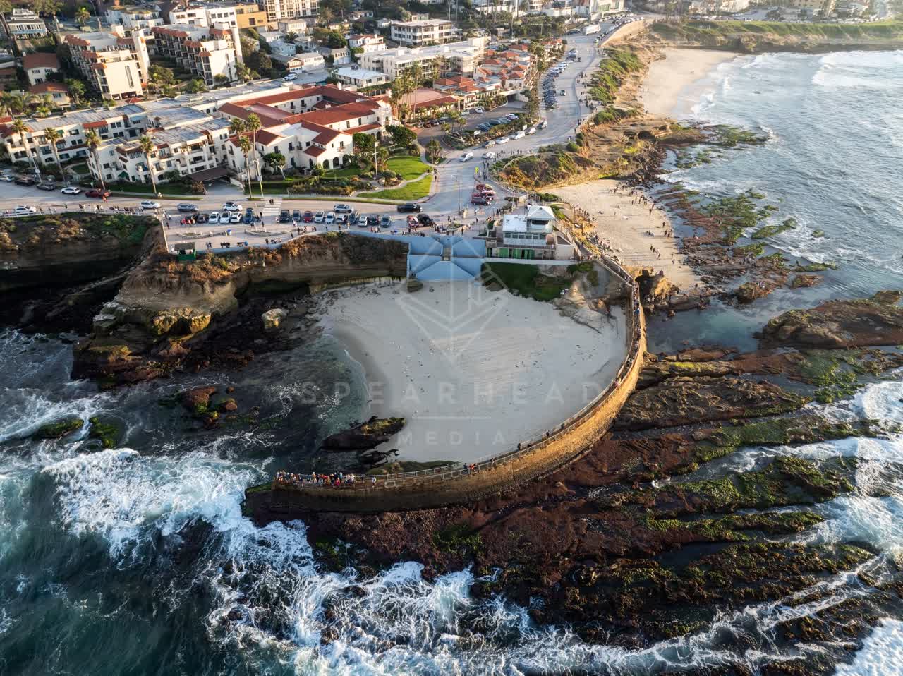 Aerial view of the cliffs, the surf and boats at La Jolla Cove, with people walking.