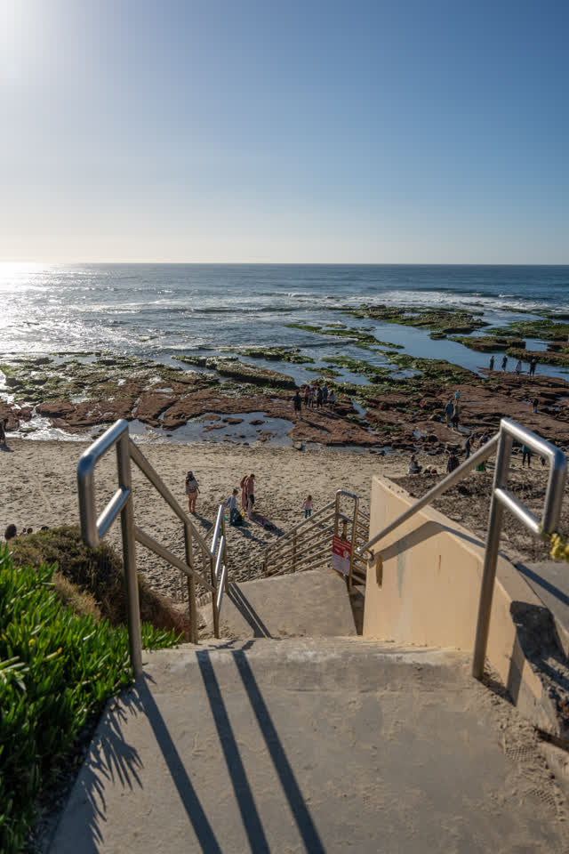 Elevated view of the beach, the ocean and the cliffs at La Jolla Cove, with people walking.