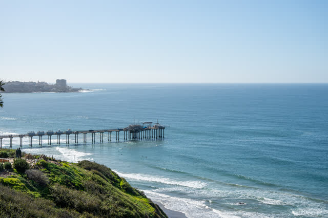 Elevated view of the cliffs, the pier and the ocean at La Jolla Shores, with people walking.