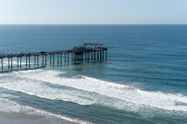 Aerial view of the beach, the surf and the pier at La Jolla Shores, with surfers out.