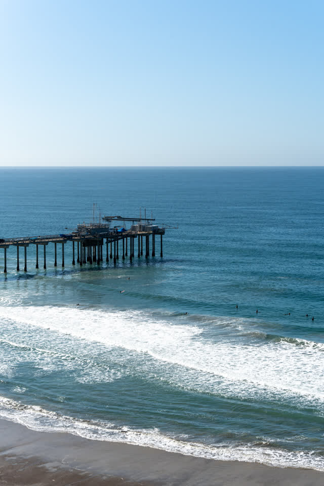 Elevated view of the beach, the surf and the pier at La Jolla Shores, with surfers out.