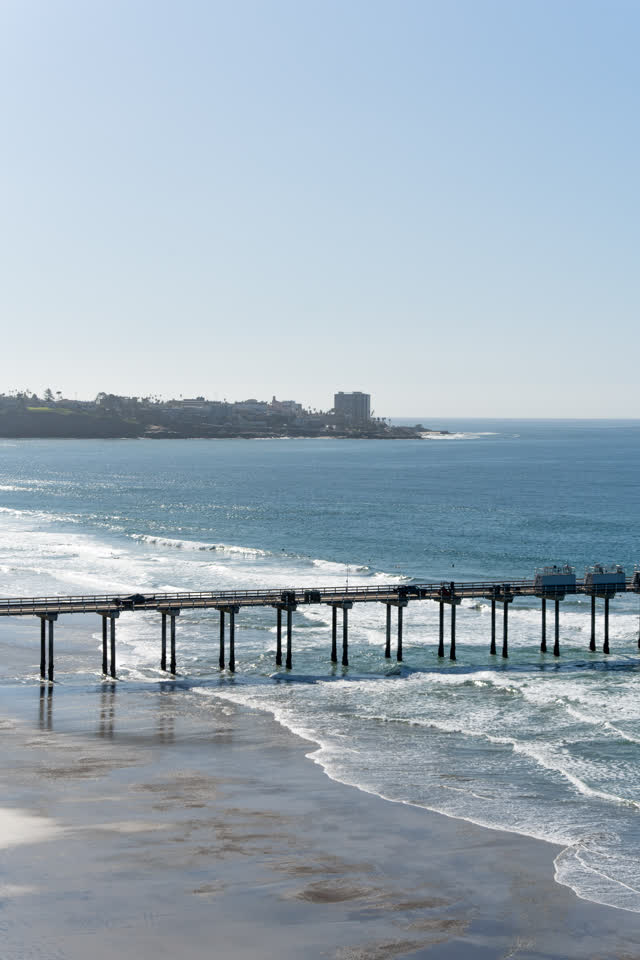 Elevated view of the beach, the surf and the pier at La Jolla Shores, with people walking.