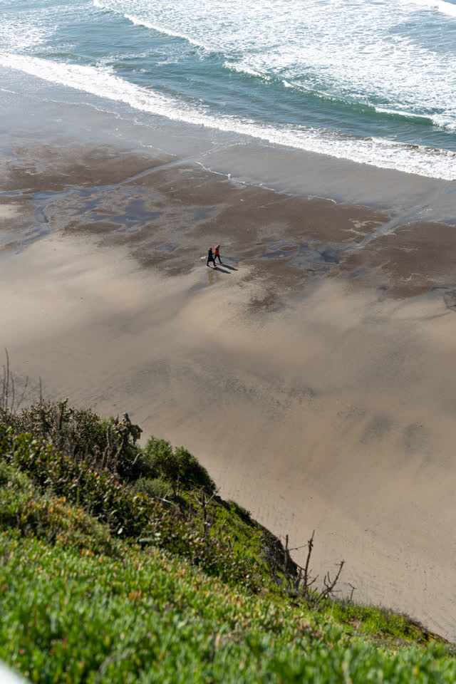 Elevated view of the cliffs, the surf and the ocean at La Jolla Shores, with people walking.