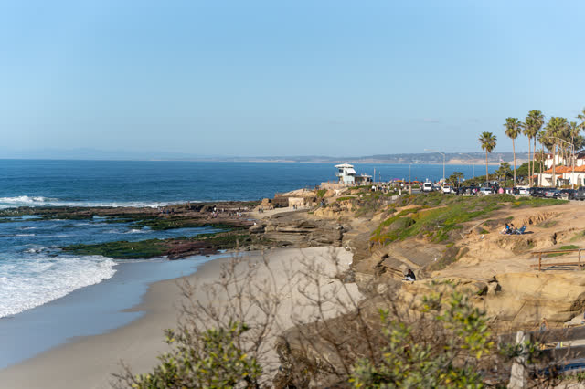 Elevated view of the beach, palm trees and the ocean at La Jolla Cove, with people walking.