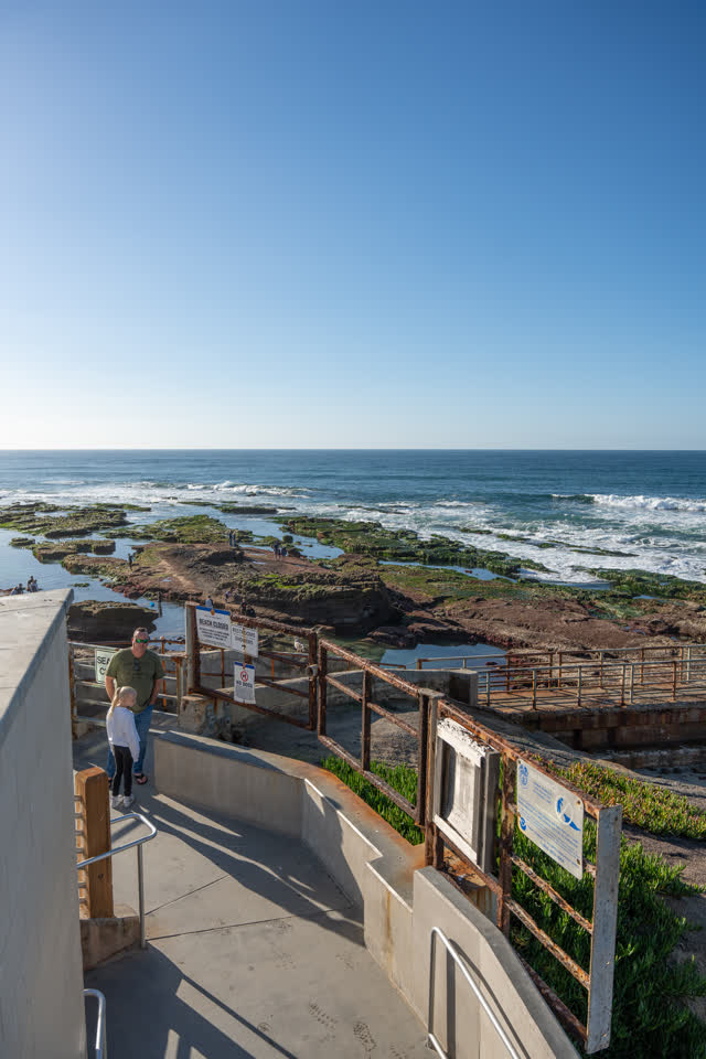 Elevated view of the cliffs, the ocean and open country at La Jolla Cove, with people walking.