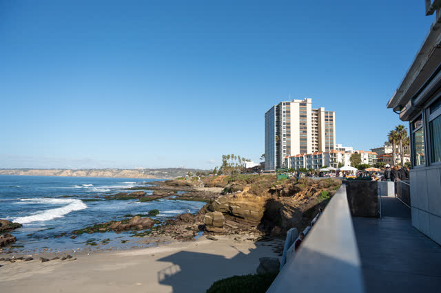 Elevated view of the beach, palm trees and the ocean at La Jolla Cove, with a crowd gathered.