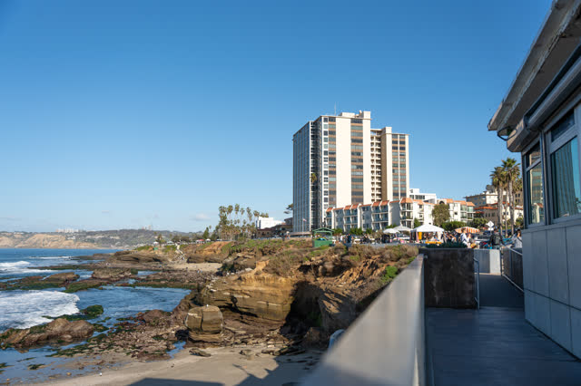 Elevated view of the cliffs, palm trees and the ocean at La Jolla Cove, with a crowd gathered.