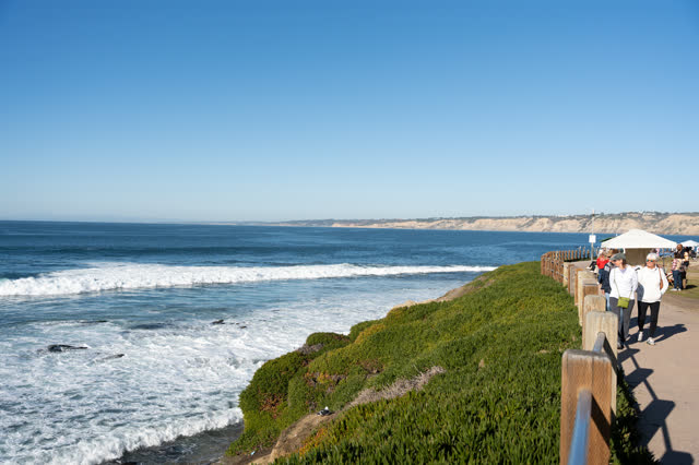 Elevated view of the cliffs, the surf and the ocean at La Jolla Cove, with people walking.