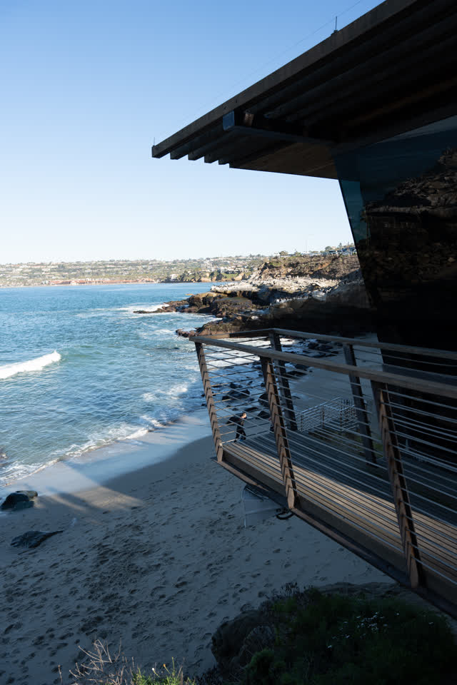 Elevated view of the cliffs, the surf and the ocean at La Jolla Cove, with people walking.