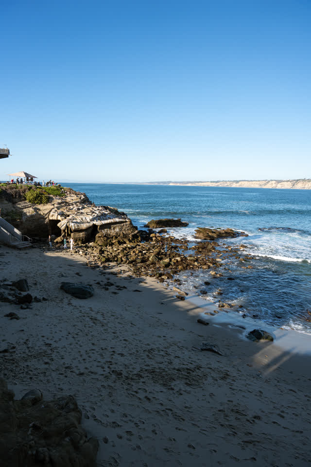 Elevated view of the beach, the ocean and the cliffs at La Jolla Cove, with people walking.