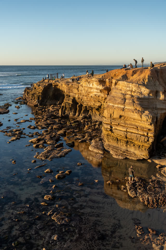 Elevated view of the cliffs, the surf and the ocean at Sunset Cliffs, with people walking.