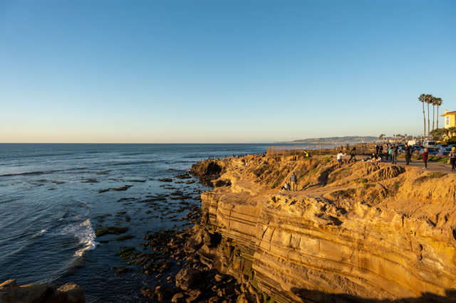 Elevated view of the cliffs, palm trees and the ocean at Sunset Cliffs, with a crowd gathered.