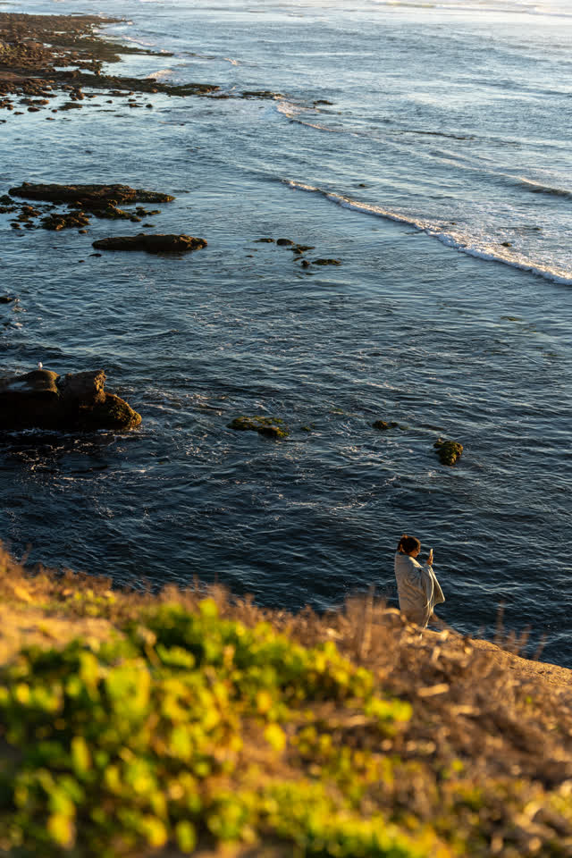 Elevated view of the cliffs, the surf and the ocean at Sunset Cliffs, with people walking.