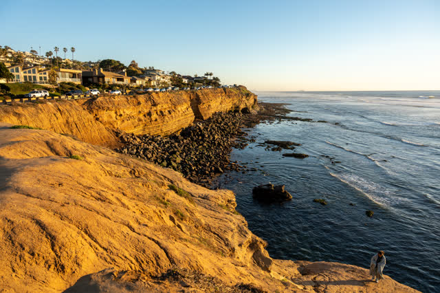 Elevated view of the cliffs, palm trees and the ocean at Sunset Cliffs, with people walking.