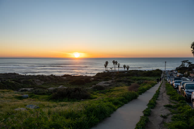Elevated view of the cliffs, palm trees and the ocean at Sunset Cliffs, with people walking.
