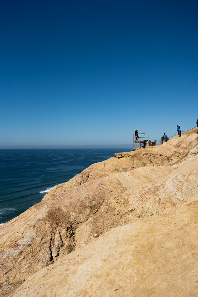 Elevated view of the cliffs, the ocean and open country at Torrey Pines, with people walking.