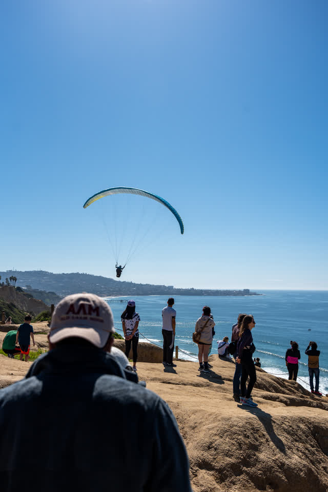 Elevated view of the cliffs, the pier and the ocean at Torrey Pines, with a crowd gathered.