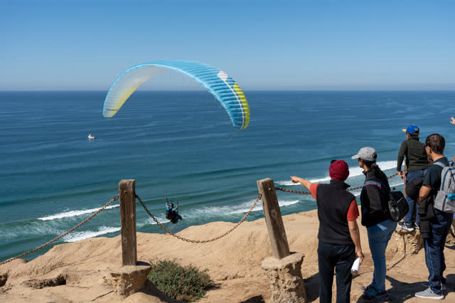 Elevated view of the cliffs, the ocean and the beach at Torrey Pines, with a crowd gathered.