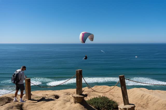 Elevated view of the cliffs, the surf and boats at Torrey Pines, with a crowd gathered.
