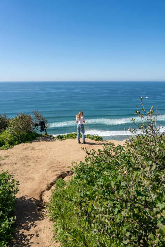 Elevated view of the cliffs, the surf and the ocean at Torrey Pines, with people walking.