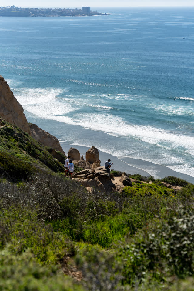Elevated view of the cliffs, the surf and the ocean at Torrey Pines, with people walking.
