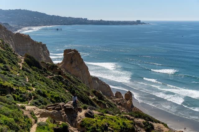 Elevated view of the cliffs, the surf and the pier at Torrey Pines, with people walking.