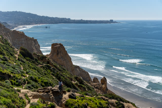 Elevated view of the cliffs, the surf and the pier at Torrey Pines, with people walking.