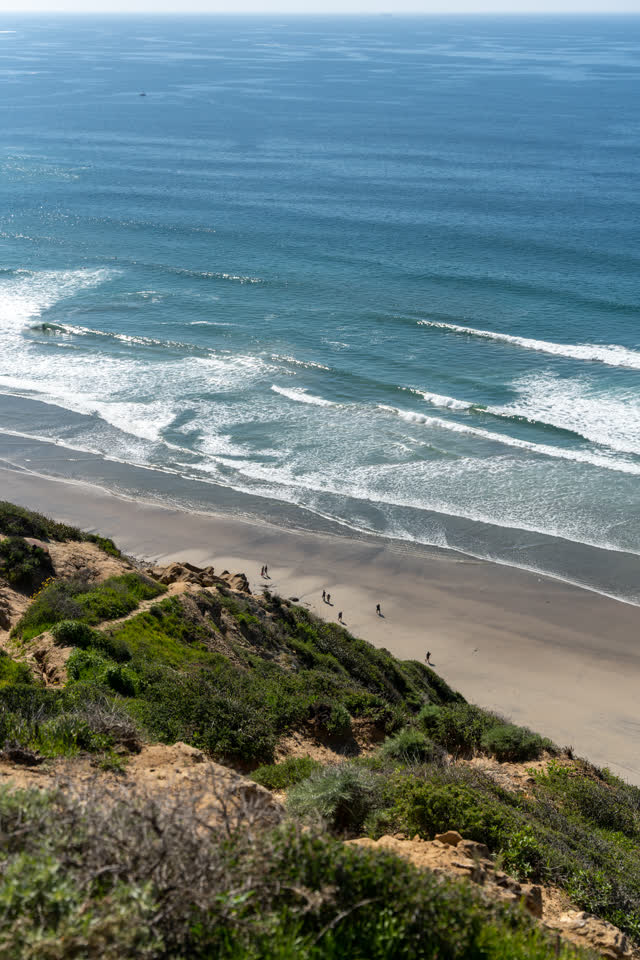 Elevated view of the cliffs, the surf and the ocean at Torrey Pines, with people walking.