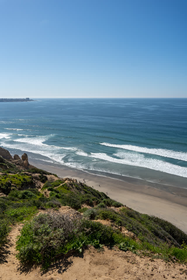 Elevated view of the cliffs, the surf and the ocean at Torrey Pines, with people walking.