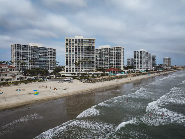 Low aerial view of the beach, the surf and palm trees at Coronado Beach, with swimmers in the water.