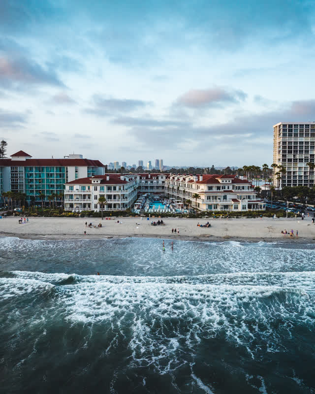 Low aerial view of the beach, the surf and the skyline at Coronado Beach, with people walking.