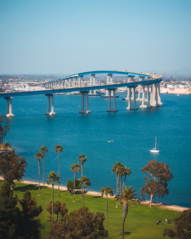Elevated view of the harbor, the bridge and boats at Coronado Beach, with people walking.