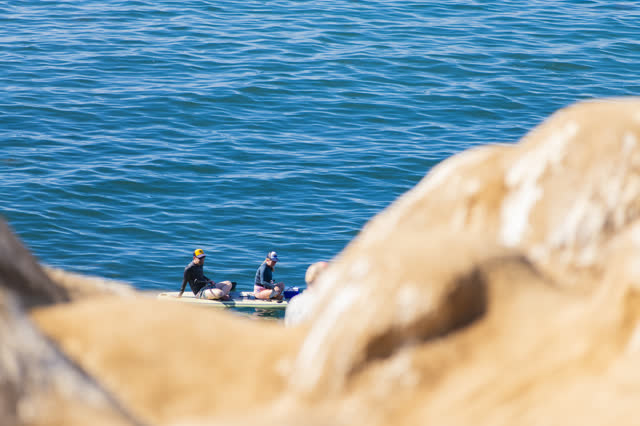 Elevated view of the cliffs, the surf and the ocean at La Jolla Cove, with paddlers on the water.