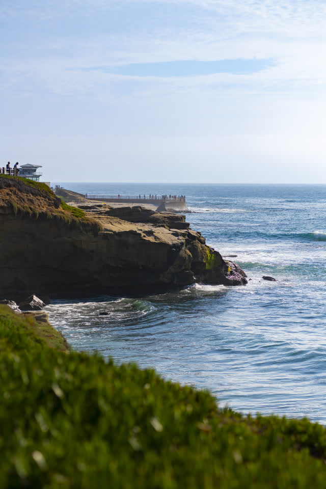 Elevated view of the cliffs, the surf and the ocean at La Jolla Cove, with people walking.