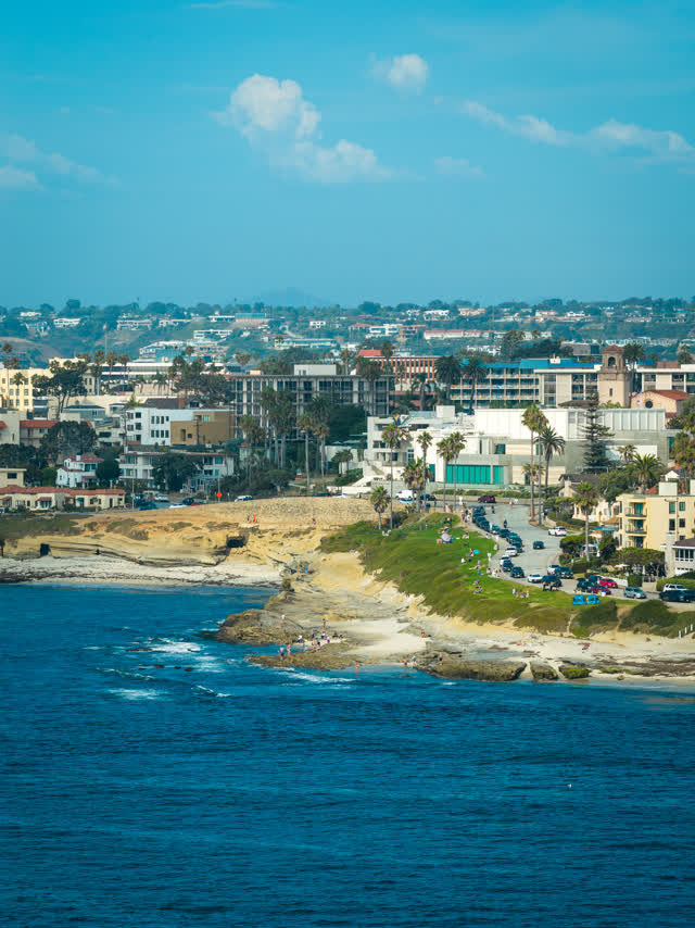 Aerial view of the cliffs, palm trees and the ocean at La Jolla Cove, with people walking.