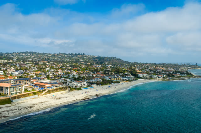 Aerial view of the beach, the ocean and homes in La Jolla, with people walking.