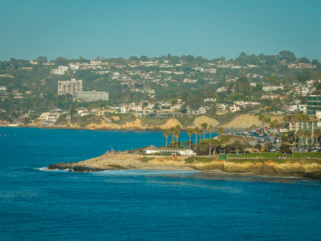 Aerial view of the cliffs, palm trees and the ocean at La Jolla Cove, with people walking.