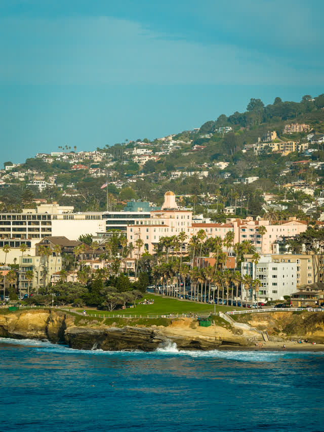 Aerial view of the cliffs, palm trees and the ocean at La Jolla Cove, with people walking.