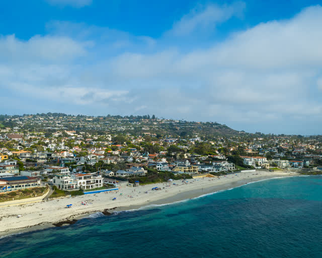 Aerial view of the beach, the ocean and homes in La Jolla, with people walking.