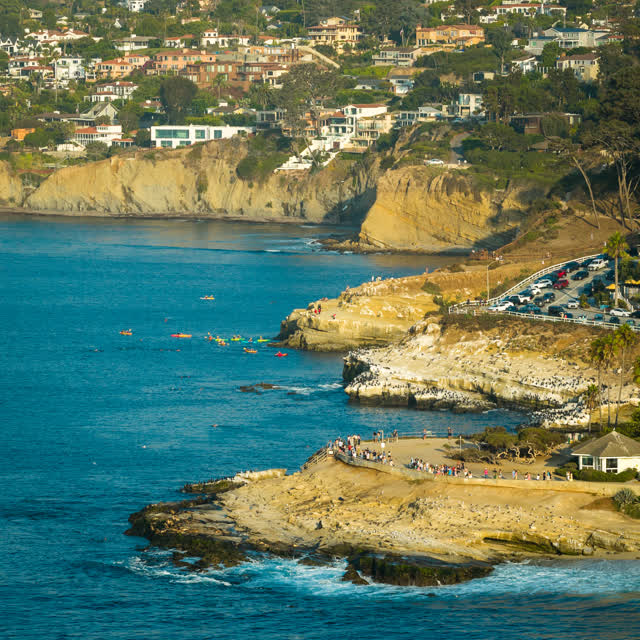 Aerial view of the cliffs, boats and wildlife at La Jolla Cove, with a crowd gathered.