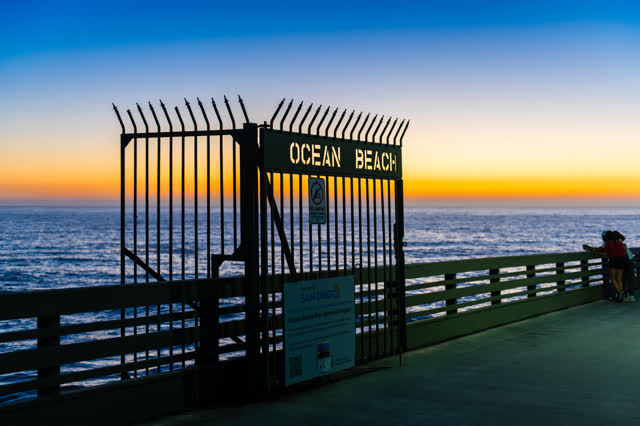 The beach, the pier and the ocean in Ocean Beach, with people walking.